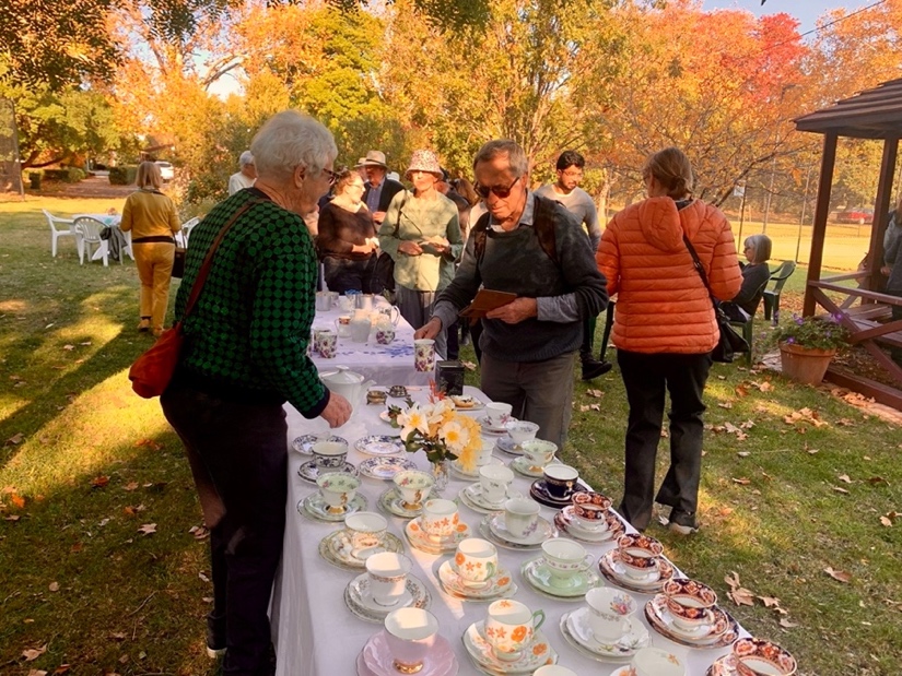 A group of people standing around a table with tea cups and saucers

Description automatically generated